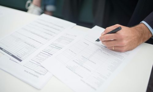 Close-up of a hand signing insurance documents in an office setting.